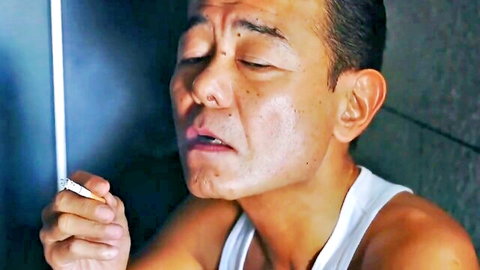 Intense Asian man in white tank top smoking cigarette in dramatic scene