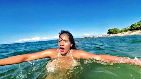 Wet Asian babe in see-through white bikini splashing arms wide in ocean waves