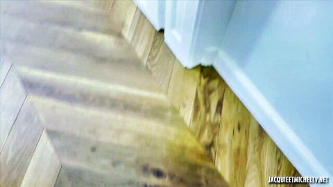 Blurry close-up of herringbone wooden floor beside white wall in adult video scene
