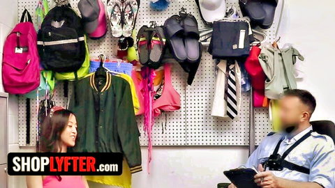 Asian shoplifter in pink smiles at blurred security officer in back office