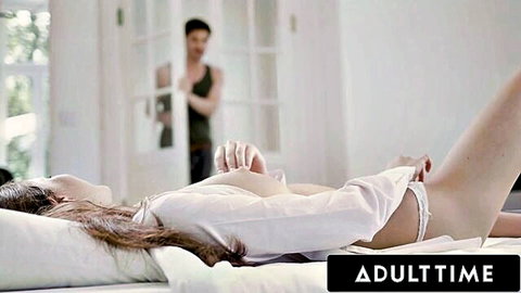 Skinny brunette babe lies on bed with open shirt exposing natural tits and spread pussy as man watches from door