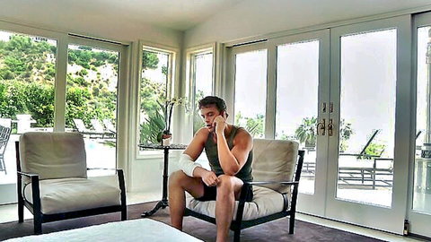 Tanned muscular man with arm cast lounging shirtless in modern living room by pool view