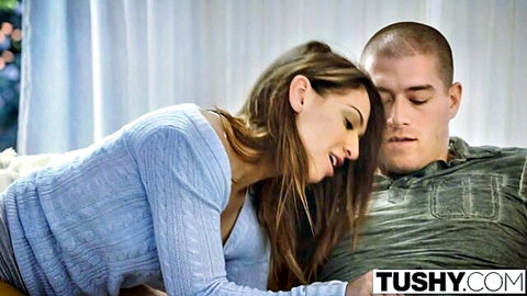 Brunette in blue sweater leans close over handsome shaved-head stud on bed