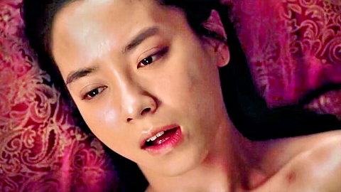 Korean beauty with parted glossy red lips and intense eyes lying sensually on ornate pink sheets