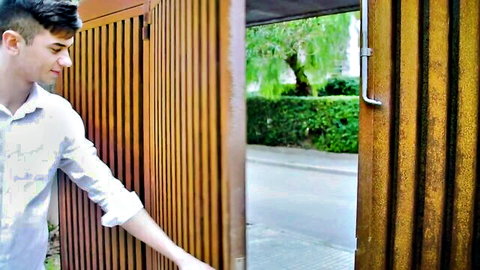 Young handsome guy in white shirt opening wooden gate outdoors