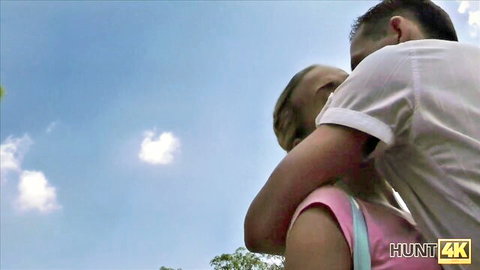 Young blonde babe in tight pink top hugged from behind by guy outdoors