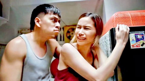 Muscular Filipino guy in tank top grabs sexy woman in red dress against kitchen fridge.