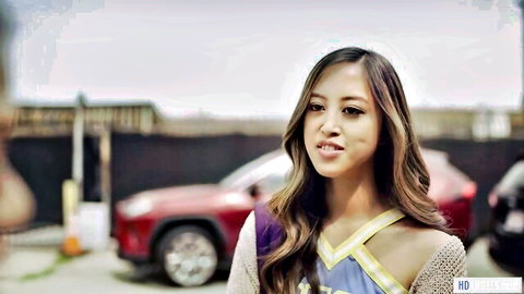Sexy Asian cheerleader in purple uniform smiles outdoors