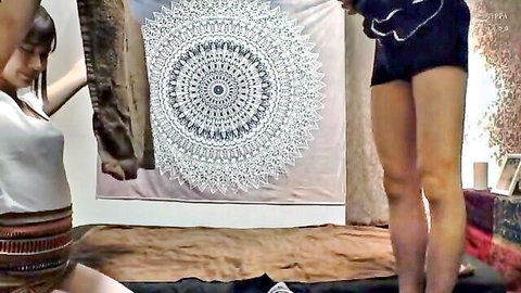 Young Asian woman in white top and black shorts posing seductively in bedroom