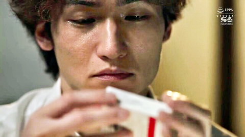 Young Japanese man in white shirt holding white pack with red stripe close to face