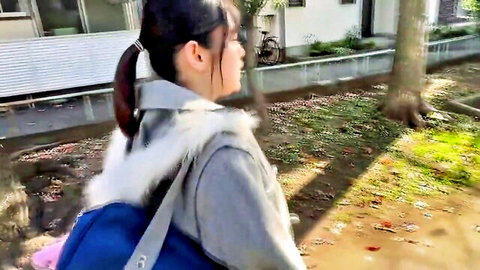 Cute Japanese schoolgirl with ponytail in fur-trimmed jacket walks outdoors carrying blue backpack