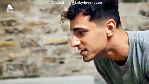 Handsome Greek man with curly hair in gray t-shirt, side profile from tied bed TV scene