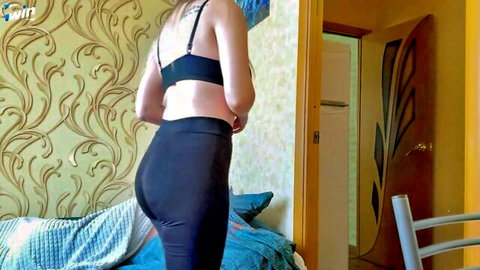 Brunette woman in black bra and tight pants posing with back view, showing curves