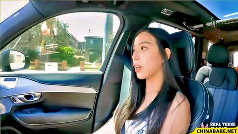 Elle Lee in car, smiling with cleavage in white top, adult tease