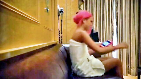 Pink-haired Asian woman in white towel, sitting solo on couch after bath