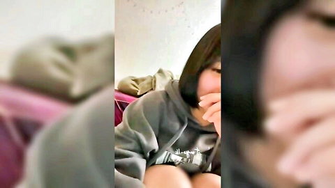 Cute Asian girl in gray hoodie smiling playfully on bed