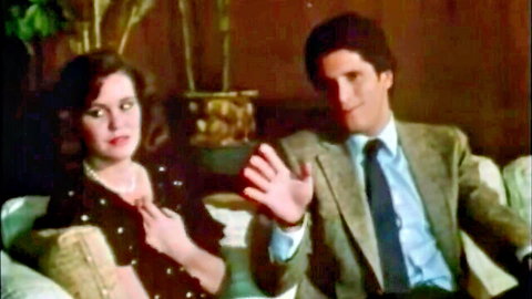 Vintage retro couple in suits and dress smiling and waving on couch in classic porn scene