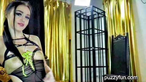 Brunette vixen in sheer black harness lingerie exposing massive tits with green straps in gold-curtained room