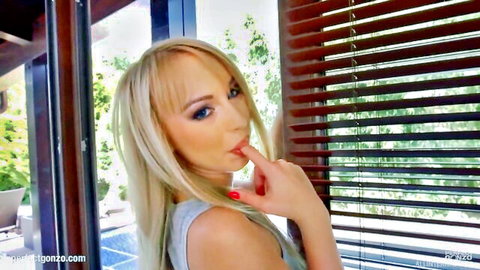 Blonde Kira Thorn seductively teasing with finger on lips in light tank top