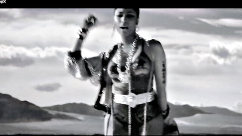 Nicki Minaj posing seductively in fringed outfit with tattoos and jewelry in desert landscape
