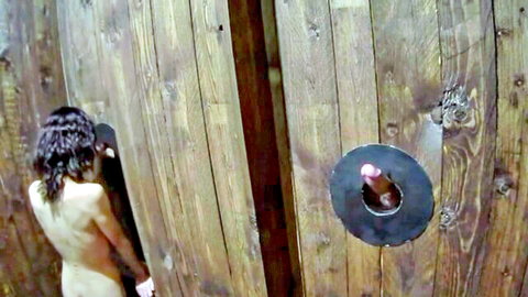 Nude curly-haired woman at glory hole with protruding dildo