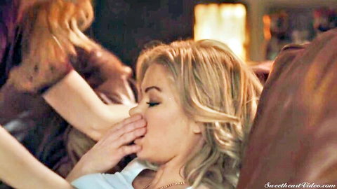 Blonde beauty passionately kissing busty brunette in intimate lesbian embrace on couch