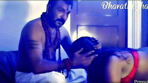 Indian man in dhoti holds woman's head in red bra, intimate bedroom pose