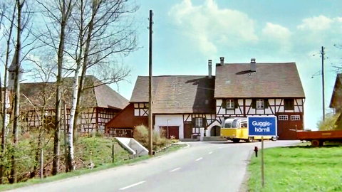 Brigitte Lahaie in scenic Swiss Alps village with half-timbered houses and vintage bus