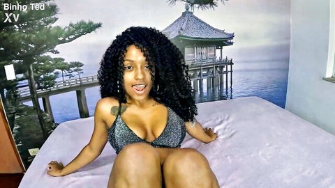 Curvy young brunette with big tits in sparkly bikini top teases with legs spread on bed