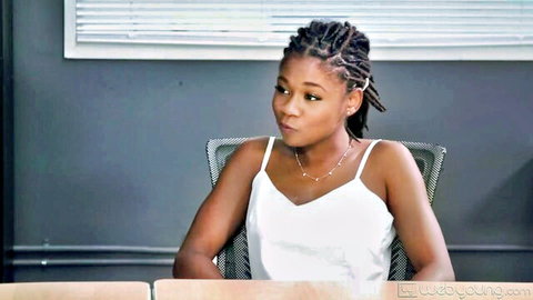 Young ebony teen with dreads and perky tits pouting in tight white tank top at office desk