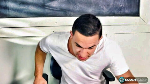 Intense Latino male teacher in white t-shirt leaning forward in classroom