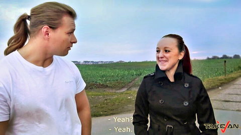 Redhead in trench coat chats with ponytail man outdoors near fields