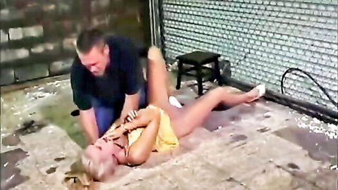 Blonde woman in yellow dress dominated by man in rough scene