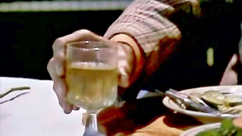 Man's hand holding whiskey glass in seductive dining scene from Mad Love 1988 classic