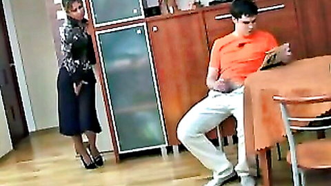 Mature mom in sexy black dress teases stepson reading at kitchen table