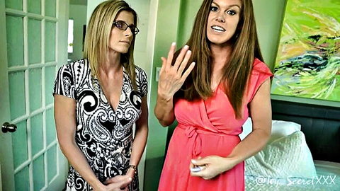Busty blonde MILF in glasses and curvy brunette in red wrap dress gesturing passionately in bedroom