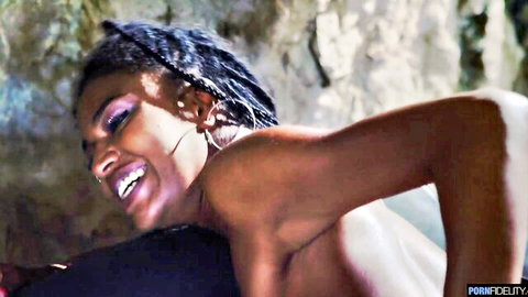 Tina Fire nude ebony beauty smiling bent over in rocky setting