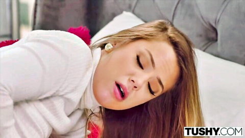 Avery Cristy in white turtleneck on bed, eyes closed in pleasure