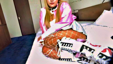 Blonde Asian woman in pink jacket, fishnets, and sneakers posing seductively on bed