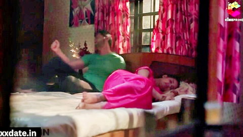 Indian bhabhi in pink dress lying on bed, man in green shirt behind her