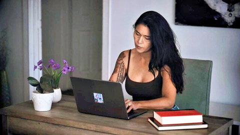 Dana Vespoli at desk in low-cut black tank top, showing deep cleavage and tattoos