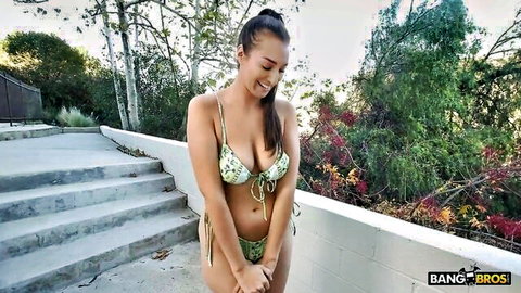 Bella Rolland in green floral bikini, smiling seductively outdoors