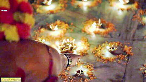 South Asian woman's hand with red bangles lighting diyas amid marigold flowers on Diwali