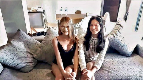 Two sexy Asian teens, one in black lace top showing deep cleavage and another in schoolgirl blouse skirt, posing on couch