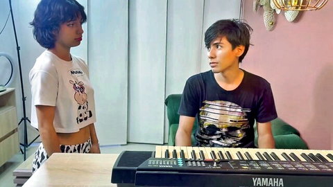 Petite Latina teen in tight cow print crop top and shorts stands by boyfriend at Yamaha keyboard