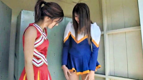 Two brunette cheerleaders in tight red and blue uniforms flirting intimately in locker room