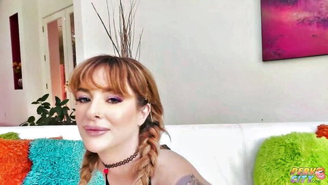 Redhead with pigtails and choker necklace poses topless on couch in teasing solo scene