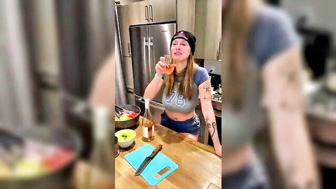 Curvy blonde babe in tight tank top with huge tits cleavage sipping orange drink in kitchen
