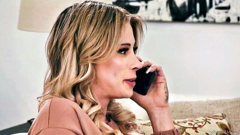 Blonde woman with long wavy hair talking on phone while sitting on couch in pink top