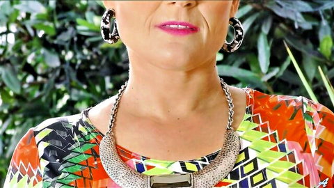 Mature woman with plump pink lips pouting seductively, big hoop earrings, chunky necklace and colorful top